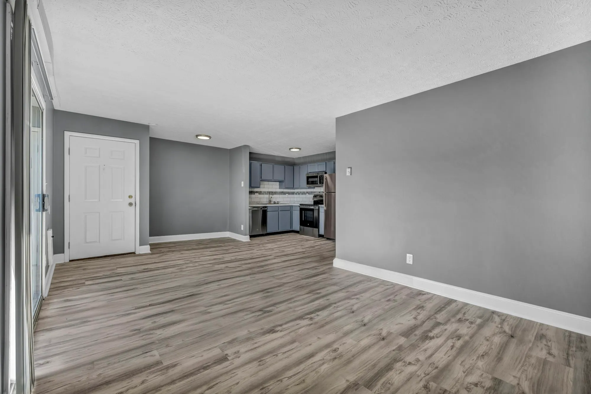 Open living area with light wood floors leading to the kitchen