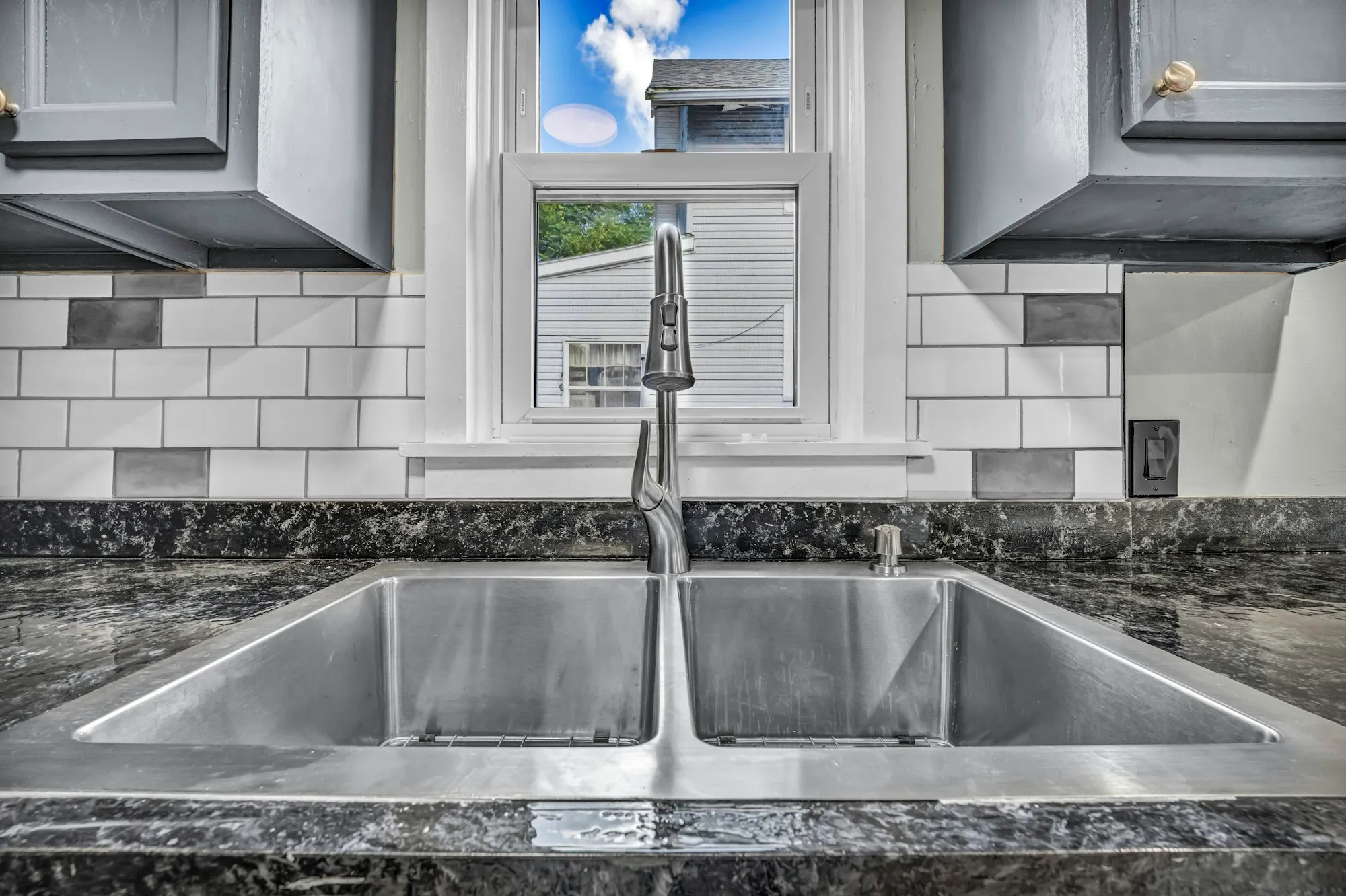 Double kitchen sink with a tall faucet under a window